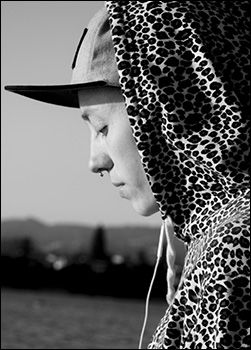 Black and white photo of Danielle Bero ’07, wearing a patterned hood and a hat, looking down. The skyline is in the background