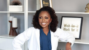 Stacy is wearing a lab coat and leaning on a shelf. 