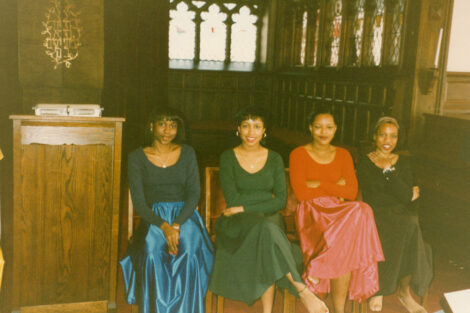 A group of four women are seated and smiling at the camera.