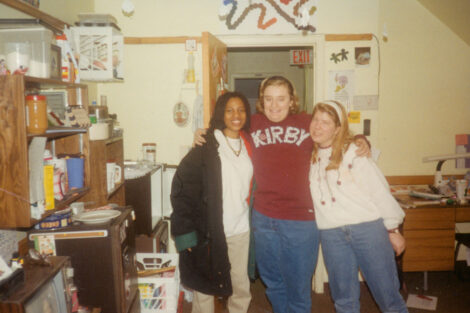 Three women are standing with their arms around each other smiling at the camera.