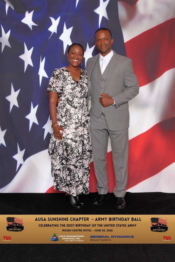 husband and wife standing in front of american flag posing for a picture