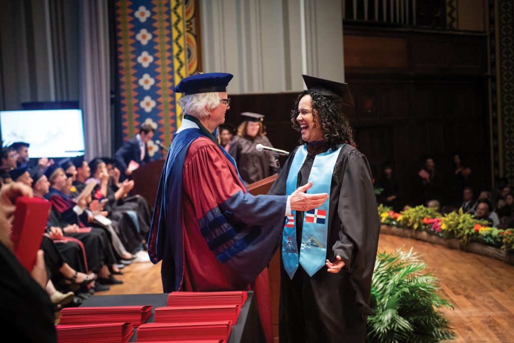 Man greeting a woman, both in caps and gowns, before she gives a speech
