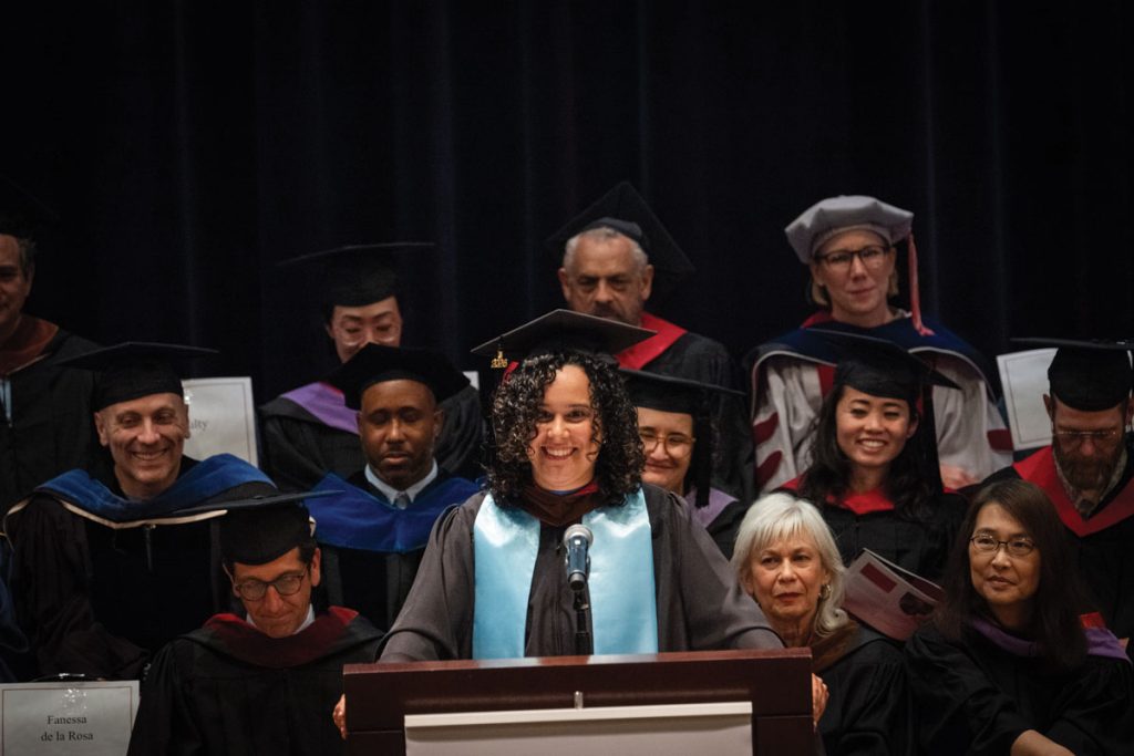 Woman standing at podium giving a speech to a crowd with onlookers behind